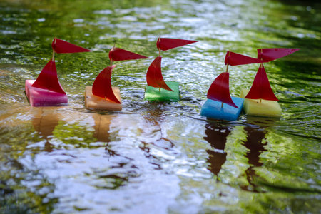 Children's ships in the summer river. Homemade boats from kitchen sponges with masts. Mock sports...