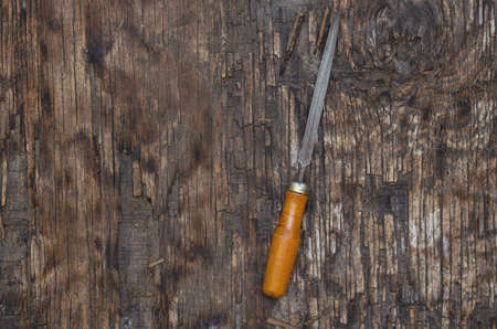 Metal file on a wooden background. An old triangular file with a wooden handle. Cracked wooden surface with cracks and splinters. top view. selective focus.の写真素材