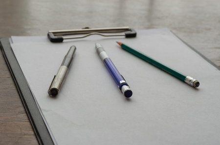 Ink pen, pen, wooden pencil and clipboard. Brown wooden desk. close-up. selective focus. no people.