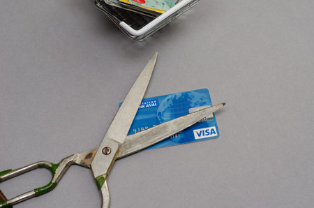 Rusty scissors and bank cards in a shopping cart against a gray background. The scissors lie on top...