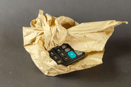A black calculator wrapped in crumpled paper. The wrapping paper is tied in a knot. close-up. selective focus.の写真素材