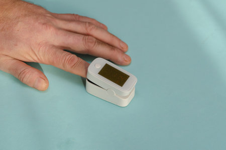 A man's hand with an oximeter on his index finger. A mature man measures capillary blood oxygen levels and heart rate. Health and Medicine. selective focus.の写真素材
