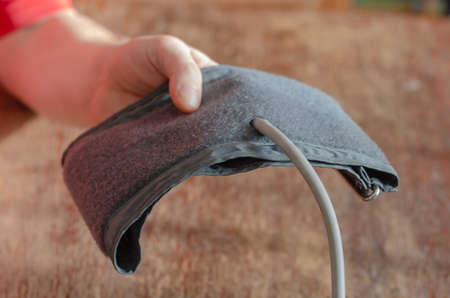 A man lends a hand into the camera with the cuff of a digital blood pressure monitor. Measuring blood pressure at home. inside the room. selective focus.の写真素材