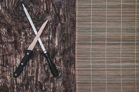 Old kitchen knife, Honing steel and bamboo cloth on dark wooden background. Cracked wooden surface...