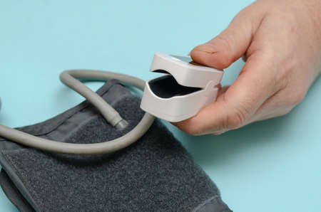 A hand holds an open white oximeter. A cuff digital blood pressure monitor lies nearby. Health and Medicine. selective focus.の写真素材