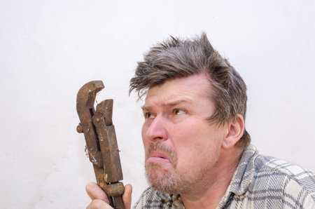 Portrait of a funny geezer with a rusty old dirty pipe wrench. An unshaven man with a hand tool...