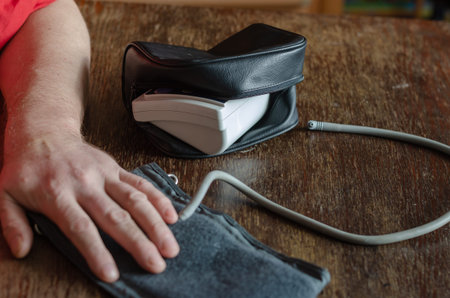 Measuring your blood pressure at home. An adult male holds the cuff of a digital blood pressure...