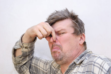 The man covers his nose with his fingers. An unpleasant smell. A male with disheveled hair faces the...