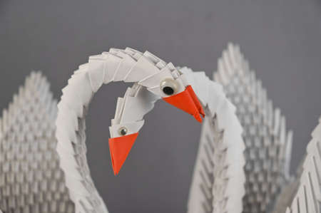 A pair of origami swans against a gray background. Two birds assembled from white triangular pieces of paper. A symbol of family, love, loyalty and devotion. selective focus.の写真素材