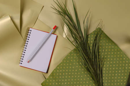 An open blank notebook and a pencil. A palm tree wreath and a green piece of paper against a beige background. Angled view from above. selective focus.の写真素材