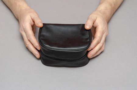 Two Hands of a middle-aged man holding a black bag against a gray background. A small closed case...