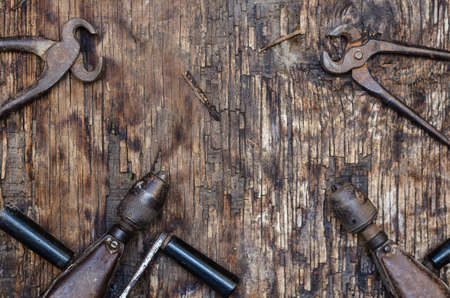 An old hand tool on a dark wooden background. metal pliers. Hand powered drilling tools and machines. Cracked wooden surface with cracks and splinters. top view. selective focus.の写真素材