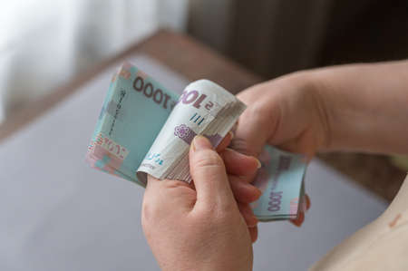 A grown woman counts money indoors. Her hands are holding a bundle of Ukrainian hryvnias. Banknotes in denominations of 1000 hryvnia. selective focusの写真素材