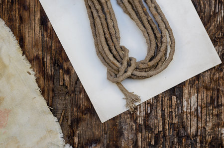 A roll of old rope, a shabby cloth, and a white piece of paper on a dark wooden background. Cracked...