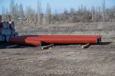 Stack of new orange polypropylene pipes in front of the railroad. Plastic pipes for laying in the...