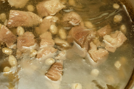 Broth with pork and white beans. Boiling soup. Pieces of meat and beans are boiled in a pot....