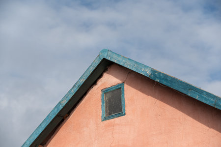 The top of the pink dwelling with a corner roof. A small structure against an overcast sky.