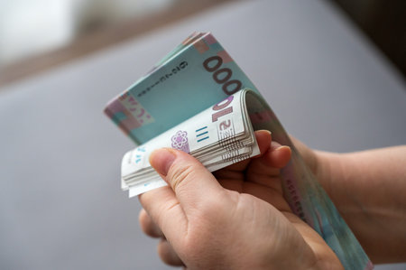 A grown woman counts money indoors. Her hands are holding a bundle of Ukrainian hryvnias. Banknotes...