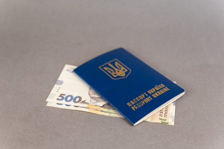 A blue covered passport and cash against a gray background. Ukrainian ID card and hryvnias.