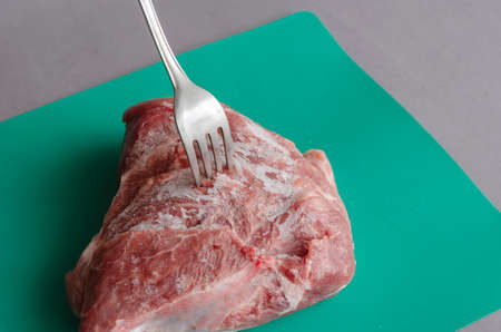 Frozen d-rump with a fork stuck on a gray-green background. A piece of pork covered in ice and frost. selective focus.の写真素材