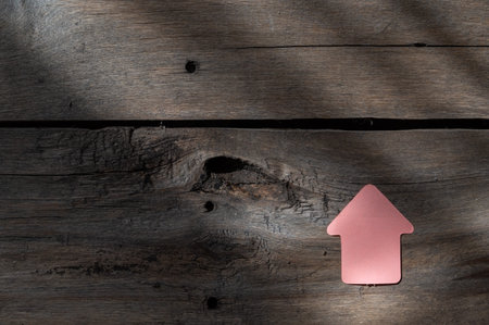 Pink paper bookmark in the shape of an arrow against a wooden background. Old wooden boards