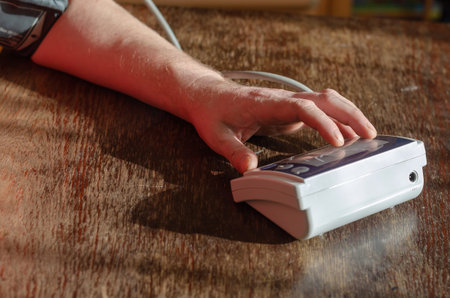 A man's hand presses the button of the digital blood pressure monitor. A medical device for...