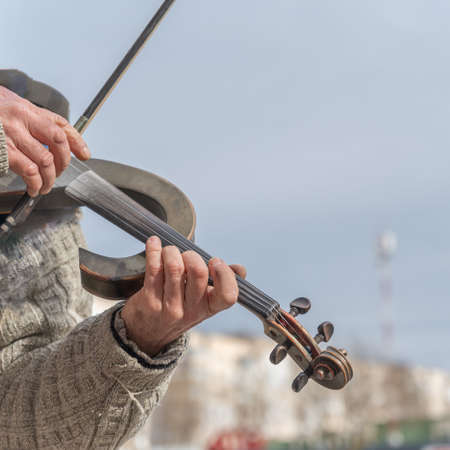 Close-up of a street musician's hands during a concert. Mature man playing electronic violin.の写真素材