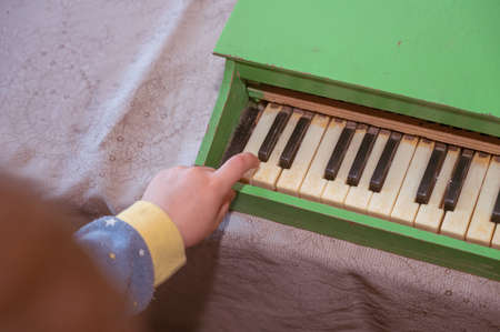 The child gently presses the piano knob with his index finger. A six-year-old boy in blue pajamas plays a child's toy piano.の写真素材