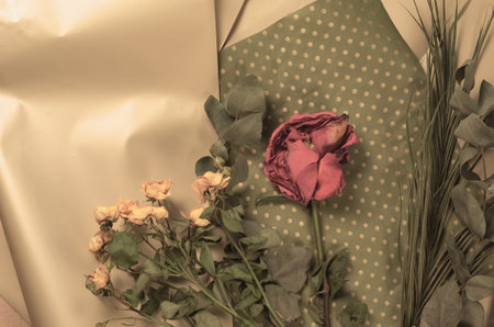 Withering flowers against a floral background. A bud of red rose and a bouquet of small yellow...
