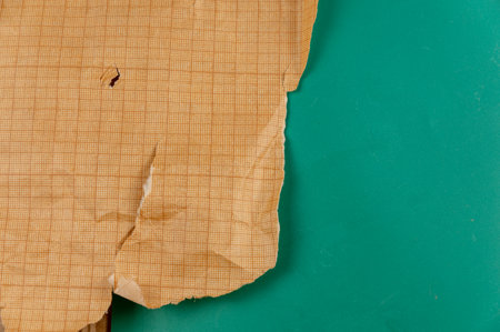 Ripped crumpled sheet of millimeter graph paper against a green background. Brown paper for drafting, design, engineering, and more. Abstract multitasking background.の写真素材