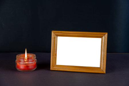 Empty horizontal photo frame and a burning candle against a dark background. Rectangular brown photo...