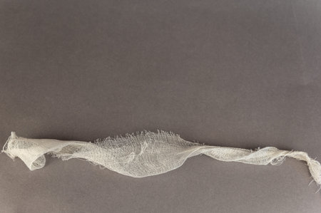 A piece of white bandage against a gray background. White gauze with an uneven jagged edge. Health...