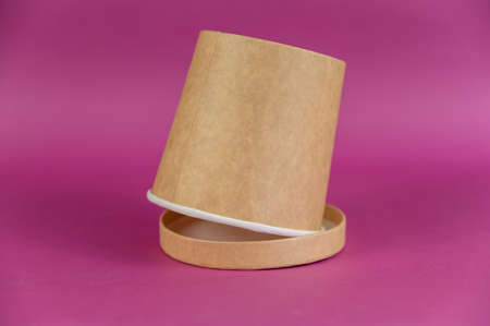 Empty cylindrical paper container with lid opposite-colored background. Brown food container for soup, ice cream, noodles, or other food.の写真素材