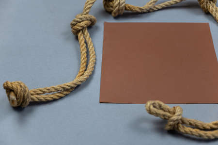 A ship's rope with knots and a brown empty square against a gray background. View from above at an angle. close-up. selective focus.の写真素材