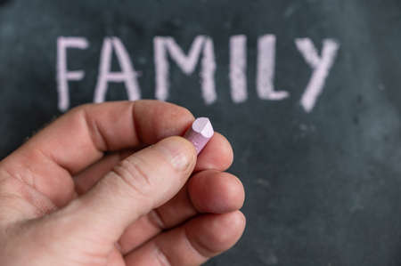 Adult male holding a piece of colored chalk in his hand. Handwritten word FAMILY on black chalkboard.の写真素材