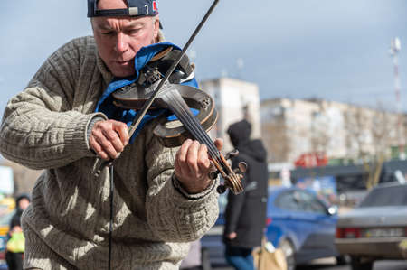 Portrait of a street musician during a concert. A mature man playing classical music on an electronic violin. Black baseball cap with Audi on his head. Ukraine, Nikolaev - 02 19 2022のeditorial素材