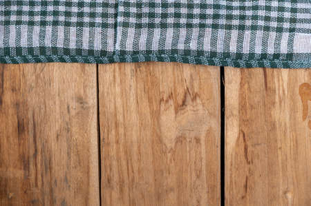 A green checkered cloth lies against a wooden background. A towel or kitchen napkin on the rough boards or kitchen table.の写真素材