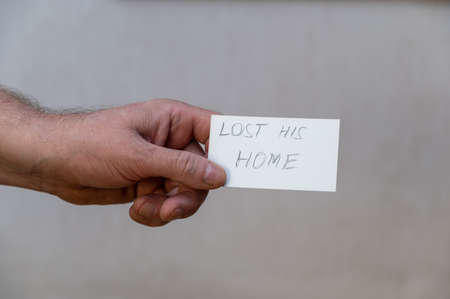 Lost his home. Words written in jagged letters. A man's hand holds a white paper rectangle with text against a gray backgroundの写真素材
