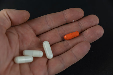 A man is holding white and orange medicine pills. The medicine lies in the open palm of an adult's...