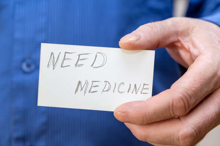 need medicine. Man holding a white paper rectangle with handwritten text. Close-up of a mature man's hand.の写真素材
