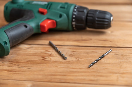 An electric drill and two drills lie against the wooden surface. The hand-held power tool is turning the boards. selective focus. no people.の写真素材