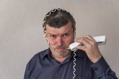 Portrait of a grown man wrapping a telephone cord around his head. A man in a blue striped shirt...