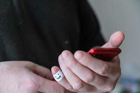 A man is holding a red smartphone. The first phalanx of his little finger is wrapped in white...