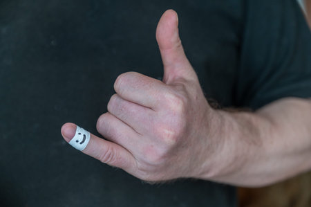 The man shows his hand a thumbs-up gesture. The first phalanx of his little finger is wrapped in...