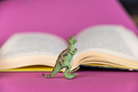 Dinosaur and open book against purple background. Green plastic miniature of an animal of prey....