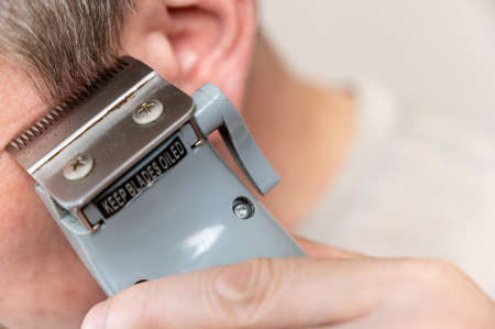 A mature man gets his hair cut. A man cuts his hair with a haircutting clipper. Hair cutting sideburns. close-up. selective focus.の写真素材