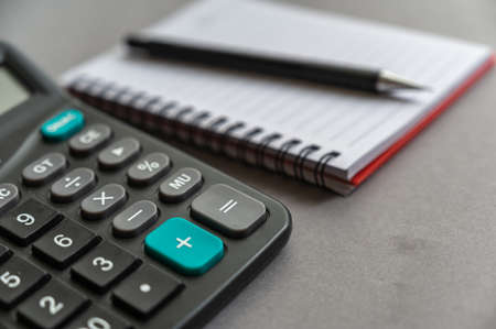 Calculator, pen, notepad lie on a gray surface. Open spring-loaded notebook with blank sheets. close-up.の写真素材