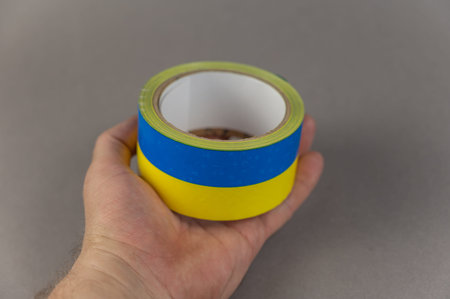 A man is holding yellow and blue duct tape in his hand. Reel of colored duct tape against the gray...