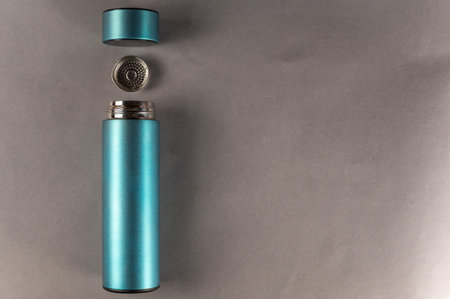 A turquoise metal flask wit lid and teapot lies against the gray background. A cylindrical vacuum...