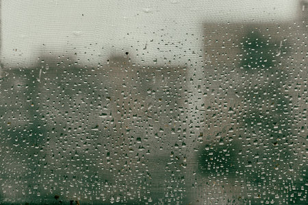 Raindrops on the mosquito net. Silhouettes of high-rise buildings blurred in the background. A...